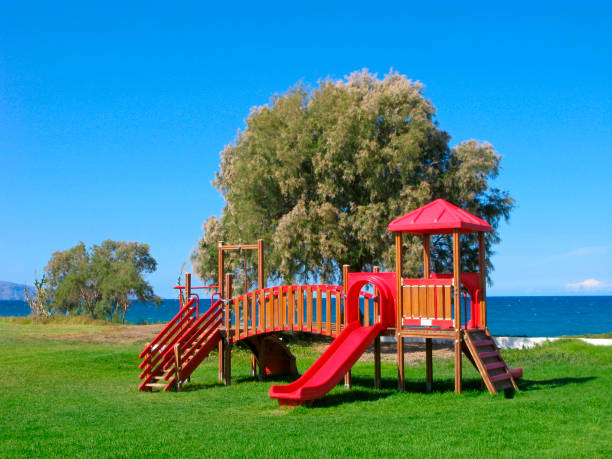 Children playground by sea. Green grass on playing field and tamarisk trees on beach. Sunny day and clear blue sky.