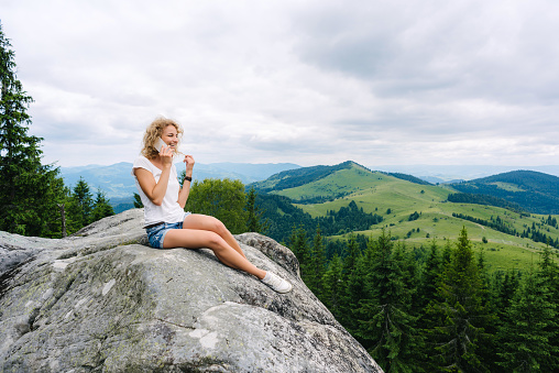 Woman talking on the phone at the top of a mountain sitting on a rock