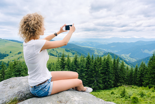 Beautiful woman hiker taking photo with cellphone on mountain top