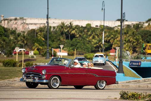Havana, Cuba - January 20, 2017: A red convertible drives near the malecon on a sunny day.