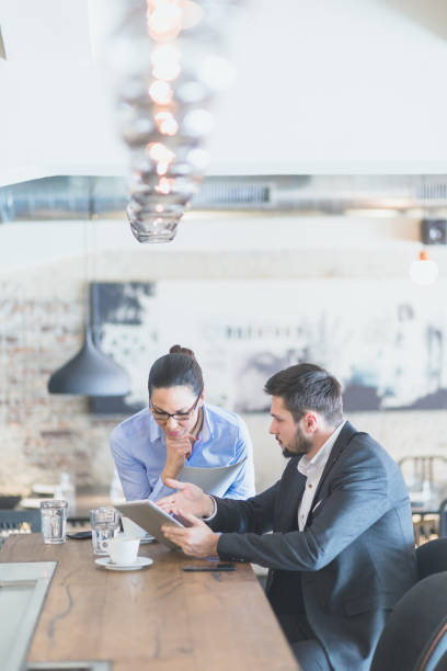 istock Handsome, young  businessman, sitting in a bar, drinking coffee, browsing tablet with his associate, young and beautiful business woman 660069772