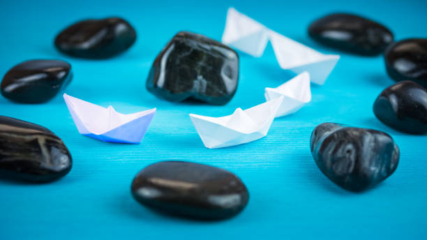 istock White paper boats in sigle file between abstract rock stones on blue background 660123976