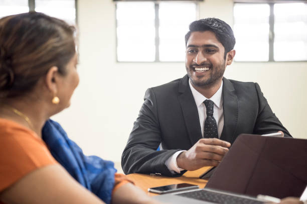 Young man in suit talking and smiling to woman with laptop Sri Lankan businessman in meeting with mature woman in office sri lanka business stock pictures, royalty-free photos & images