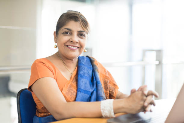 Portrait of mature Sri Lankan woman in office Woman wearing sari sitting at desk with laptop, hands clasped sari stock pictures, royalty-free photos & images