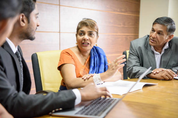 Sri Lankan woman in business meeting and young man with latop Mature woman explaining in office, man using computer in foreground, senior man listening to woman as she gestures towards colleague sri lanka business stock pictures, royalty-free photos & images