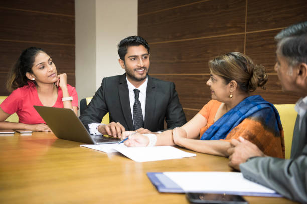 Business colleagues in meeting room, young man with laptop Four Sri Lankan business people at meeting table with paperwork sri lanka business stock pictures, royalty-free photos & images