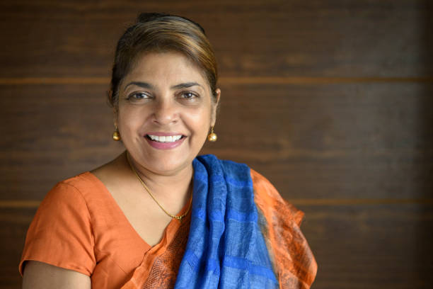 Mature woman wearing traditional sari, smiling toward camera Portrait of Sri Lankan woman in her 50s with orange dress and blue scarf sri lanka business stock pictures, royalty-free photos & images