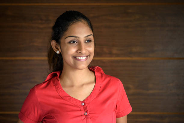 Cheerful young woman smiling and looking away against brown background Happy Sri Lankan woman in pink blouse looking off to the distance with smile on her face sri lanka business stock pictures, royalty-free photos & images