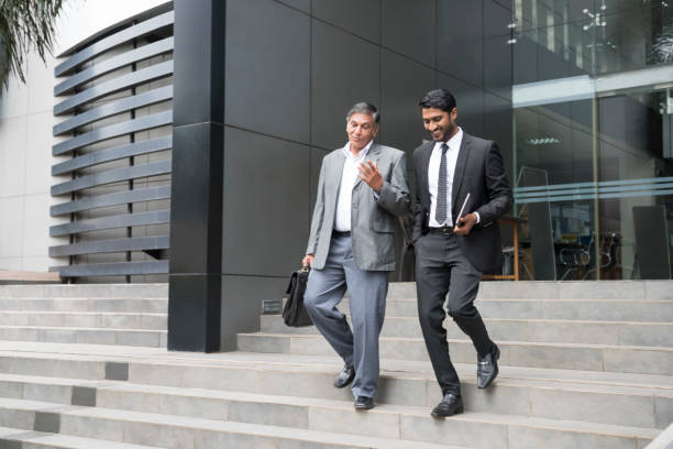 Senior businessman an young male colleague leaving offices Two businessmen walking down steps outside modern building, they are discussing and smiling with cheerful and relaxed expressions sri lanka business stock pictures, royalty-free photos & images