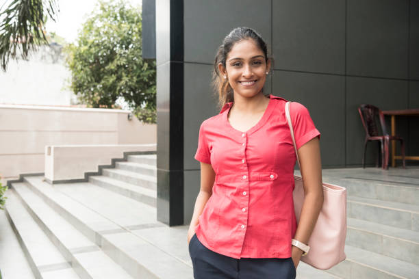 Young office worker in pink blouse and hands in pockets She is standing outside modern office building with handbag on shoulder, smiling towards camera sri lanka business stock pictures, royalty-free photos & images