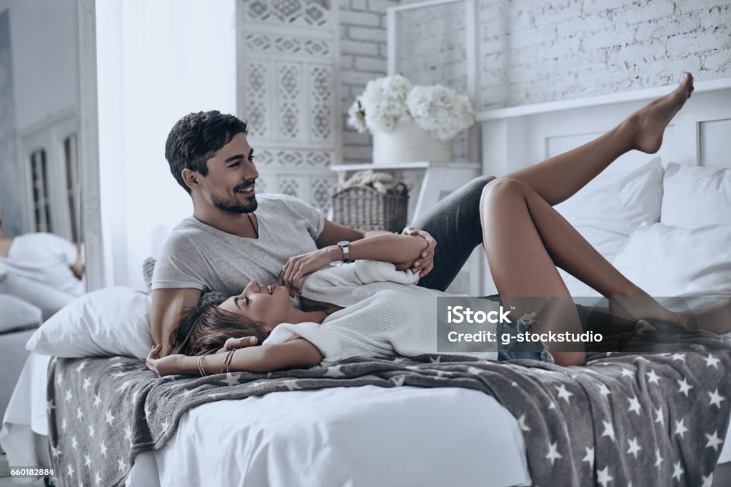 Feeling playful. Beautiful young couple lying on bed at home and smiling while spending free time at home Couple - Relationship Stock Photo
