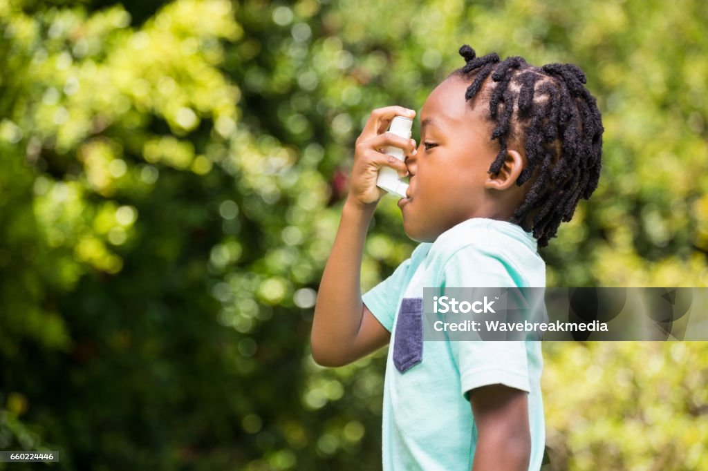 Boy using an asthma inhaler Boy using an asthma inhaler in the park Asthmatic Stock Photo