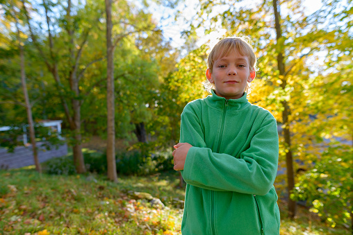 Handsome boy standing with arms crossed against sunray on path in nature park with autumn trees