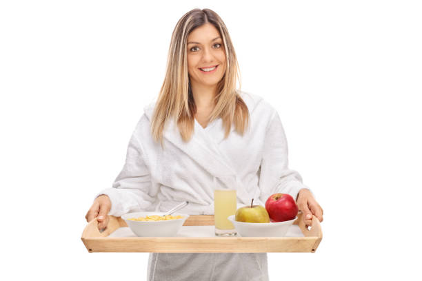 Pretty young woman wearing a bathrobe and holding a breakfast tray isolated on white background