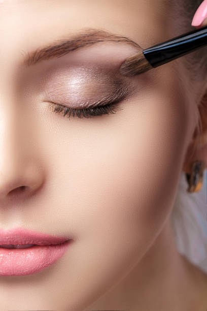 beautiful woman applying brown eye shadow using makeup brush. makeup for blue eyes