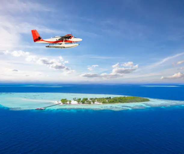 Seaplane flying above small tropical island on Maldives, aerial view. Travel, vacation, transportation and beach holiday concept