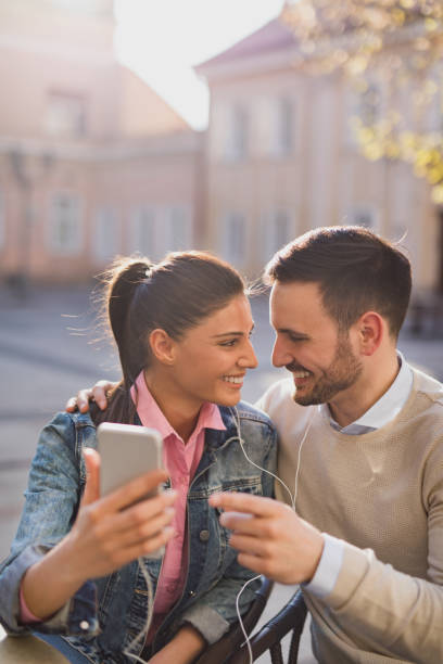 young couple surfing the net while enjoying music outdoors - surfing wireless vertical outdoors lifestyles imagens e fotografias de stock