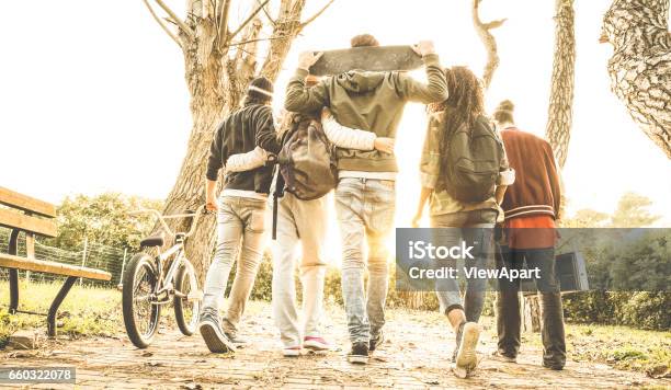 Group Of Urban Friends Walking In City Skate Park With Backlighting At Sunset Youth And Friendship Concept With Multiracial Young People Having Fun Together Warm Retro Filter With Soft Focus Stock Photo - Download Image Now