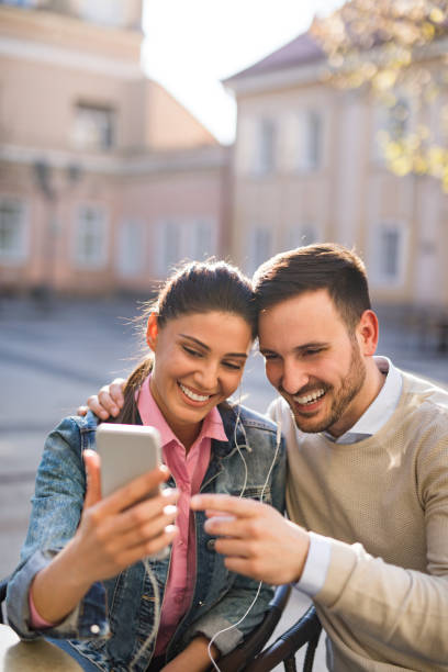 young couple surfing the net while enjoying music outdoors - surfing wireless vertical outdoors lifestyles imagens e fotografias de stock