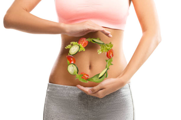 Fit, young woman holding a circle made out of vegetables over her abdomen Fit, young woman holding a circle made out of vegetables over her abdomen digestive system stock pictures, royalty-free photos & images