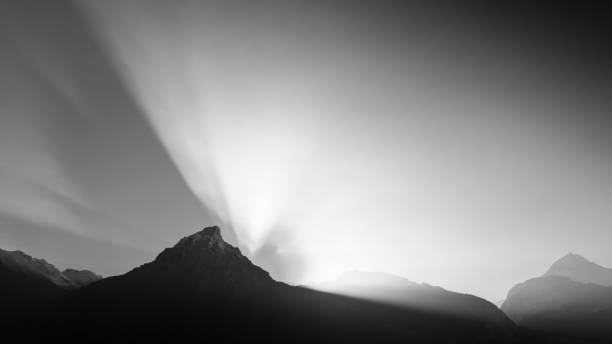 Snow capped mountain peaks in Italian Alps against a dark dramatic sky with sunbeams. Mountain range of Monte Carega (Small Dolomites). Veneto and Trentino Alto Adige, Italy, Europe.