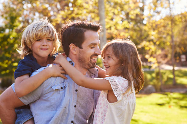 istock Father Carrying Son And Daughter As They Play In Park 660353464