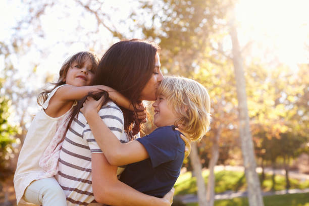 matka niosąca syna i córkę, gdy bawią się w parku - single mother one parent child kissing zdjęcia i obrazy z banku zdjęć