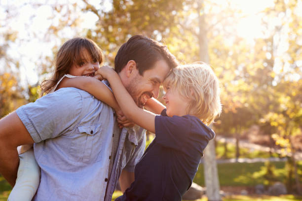 Father Carrying Son And Daughter As They Play In Park