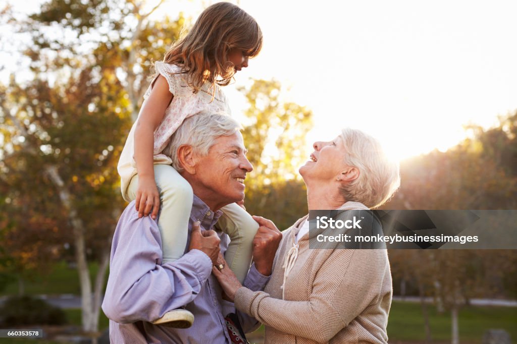 Grandparents Giving Granddaughter A Shoulder Ride In Park Grandparent Stock Photo