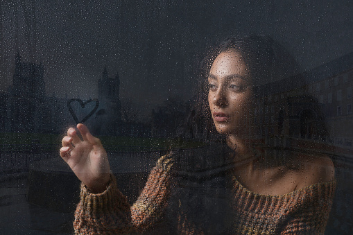 A young lady sitting at her window on a rainy day whilst daydreaming about love and romance.