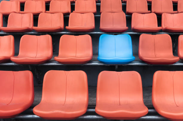 istock A blue chair amidst rows of orange plastic spectator seats. 660400084