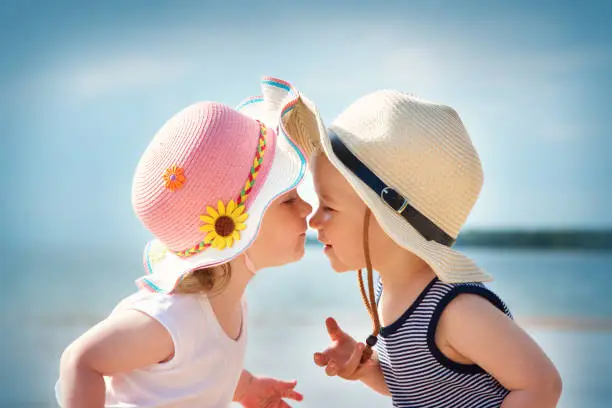 Babygirl and babyboy kissing on the beach in straw hats
