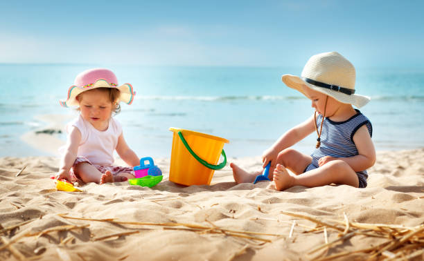 Babygirl and babyboy sitting on the beach Babygirl and babyboy sitting on the beach in straw hats beach play stock pictures, royalty-free photos & images