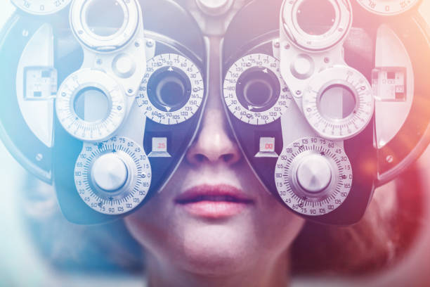 A woman's eyes are tested using a Photopter , determining whether she is due for an update in glasses prescription.  Could also depict an ophthalmologist.  Colorful lights add a futuristic feel to the image.