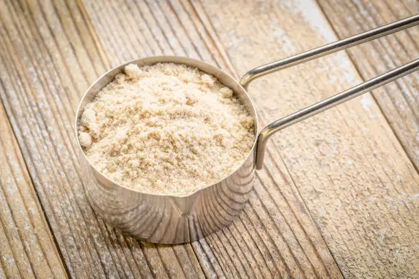 whey protein powder in a metal measuring scoop against grunge wood background