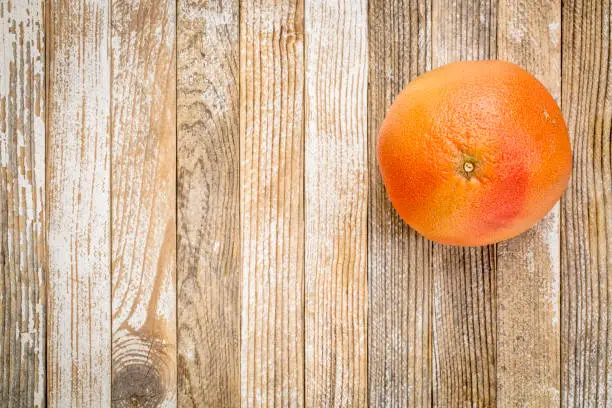 a single red grapefruit on a grunge white painted wood background with a copy space