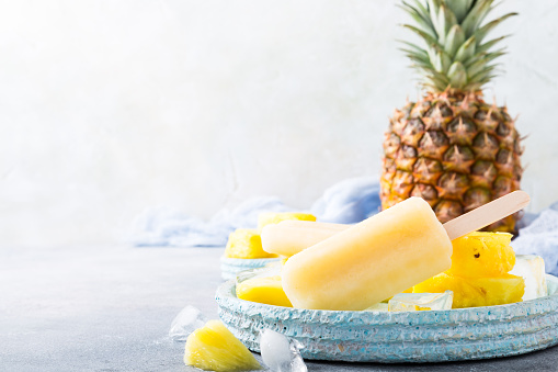 Delicious homemade pineapple popsicles on light blue plate on gray background. Summer food concept with copy space.