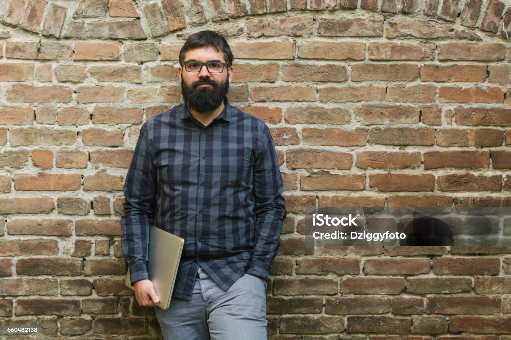 Job's done Young programmer holding laptop and standing in front of brick wall Computer Programmer Stock Photo