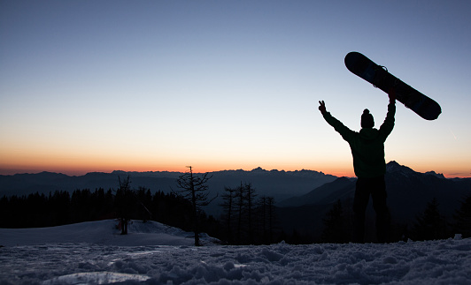 Snowboarder raising a snowboard with open arms and embracing nature in the Alps, Slovenia