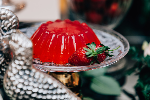Ornated gourmet red gelatin pudding dessert with strawberry fruits on luxury silver tray.