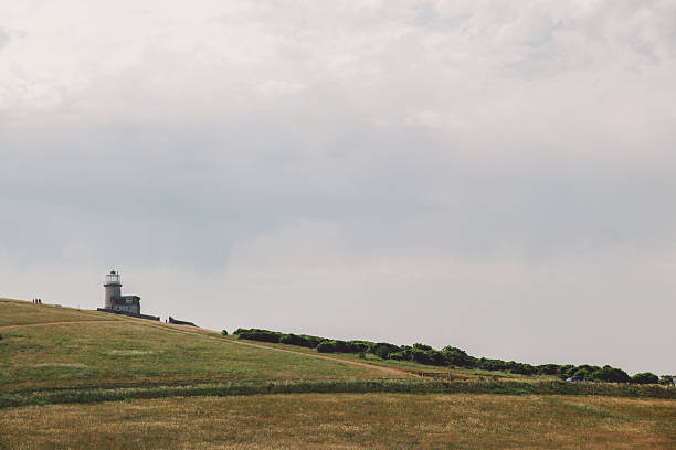 istock Distant View Of Lighthouse On Field Against Cloudy Sky 660537999