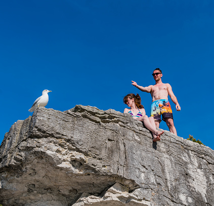 Young man and teenager girl exploring the nature, climbing on the cliff in Tobermory, lake Huron, Bruce Pennisula, Ontario, Canada