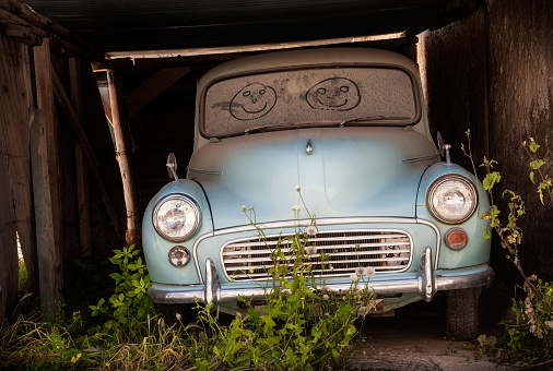 Abandoned classic car with smiling faces drawn in the dusty windscreen
