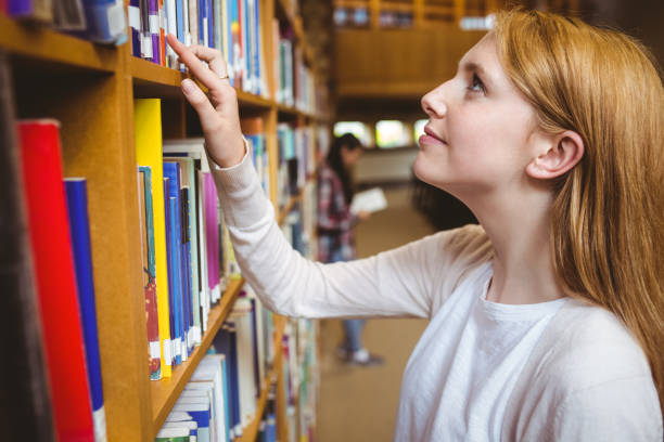istock Blond student looking for book in library shelves 660541954