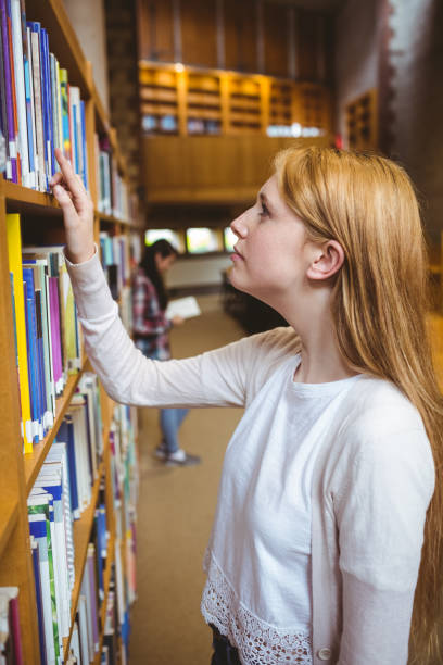 istock Blond student looking for book in library shelves 660541976