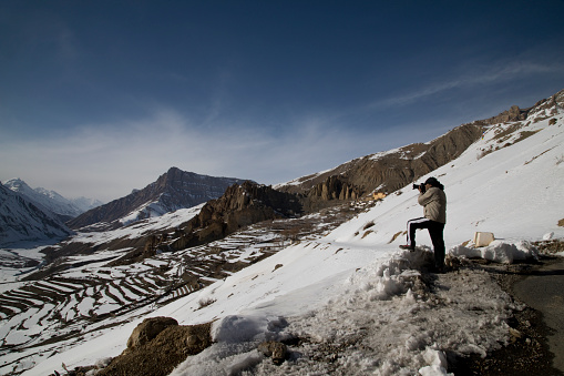 Male photographer using DSLR camera in snowcapped Himalayas mountain, Spiti, Himachal Pradesh, India