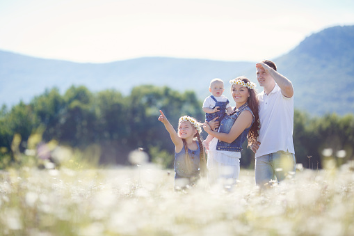 Happy family of four,mother,father,older sister and little brother spend time together in the highlands on a field of blooming white daisies in summer in the fresh air,mother and daughter wearing wreaths of flowers-white daisies