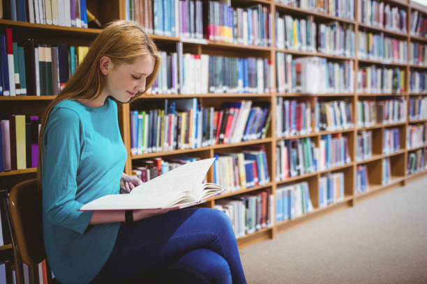 istock Smiling student sitting on chair reading book in library 660607100