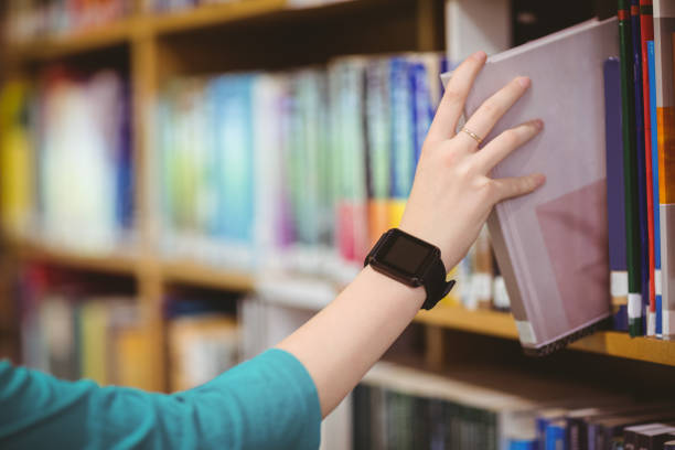istock Students hand with smartwatch picking book from bookshelf 660607220