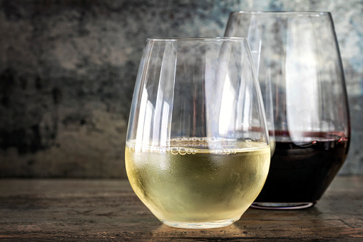 White and red wine in modern stemless glasses, with slate and timber background with copy space.